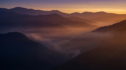 Obraz premium Misty Mountain Range at Golden Hour Panorama. Layered mountain silhouettes in purple and gold haze during sunset with dramatic fog valleys