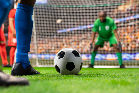 Soccer ball is positioned for a penalty kick in front of the goalkeeper, with the focused goalie guarding the target and the striker ready to shoot in a dramatic scoring attempt during the match.