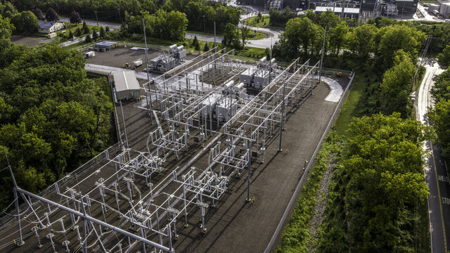 Aerial view of an electrical substation with power transformers, high-voltage busbars, circuit breakers, and steel structures surrounded by trees in Dover Plains, New York, United States.