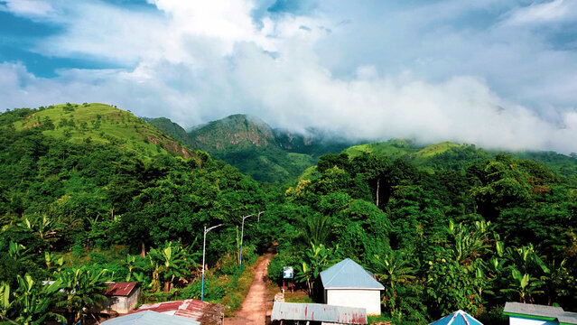 Aerial view of the lush green landscape surrounding Wli Waterfalls with dense tropical vegetation, rolling hills, and scattered buildings in Wli, Volta Region, Ghana.