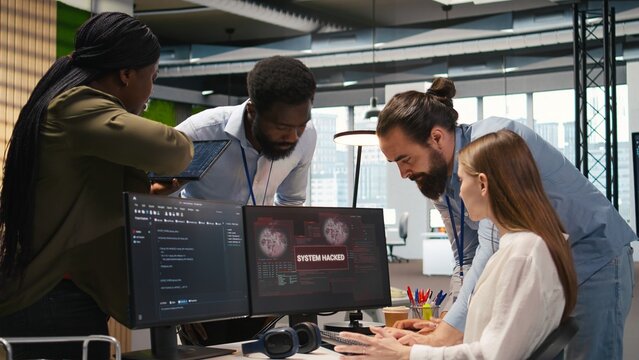 Young developer asks colleagues for help after a corporate network attack, investigating unauthorized access alerts in a startup office.