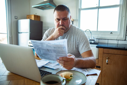Concerned man reviewing household bills at home kitchen