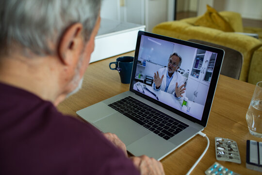 Elderly patient speaking with doctor on laptop at home