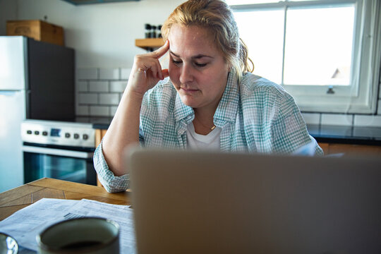 Concerned woman paying bills online at home kitchen table