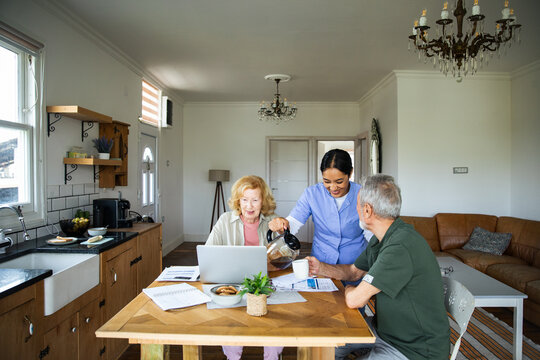 Caregiver pouring coffee for senior couple at home kitchen table