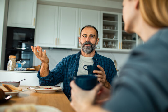 Middle-aged couple talking over coffee in home kitchen