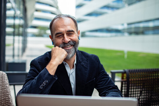 Smiling middle-aged businessman using laptop outdoors at modern office