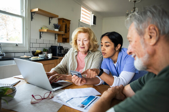Caregiver helping senior couple with online banking at home