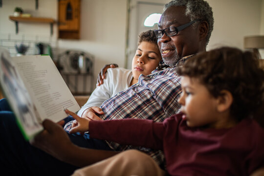 Grandfather reading storybook to grandchildren at home