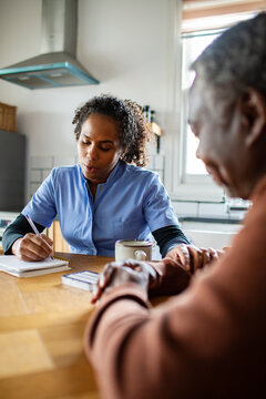 Home caregiver consulting with senior patient at kitchen table