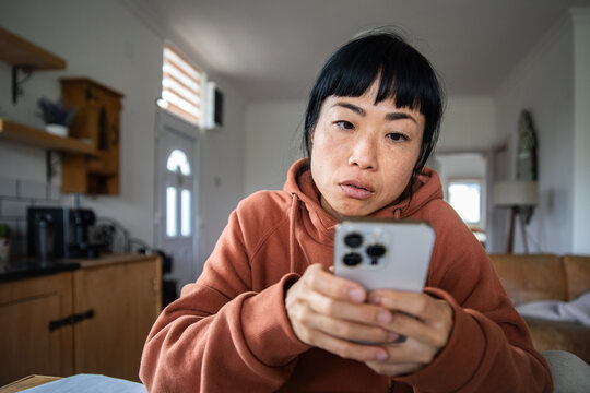 Concerned woman checking smartphone in home kitchen