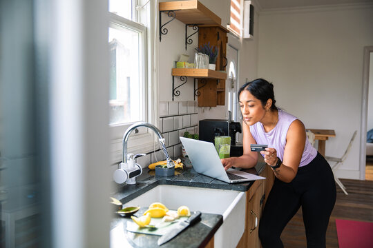 Young woman shopping online with credit card in home kitchen