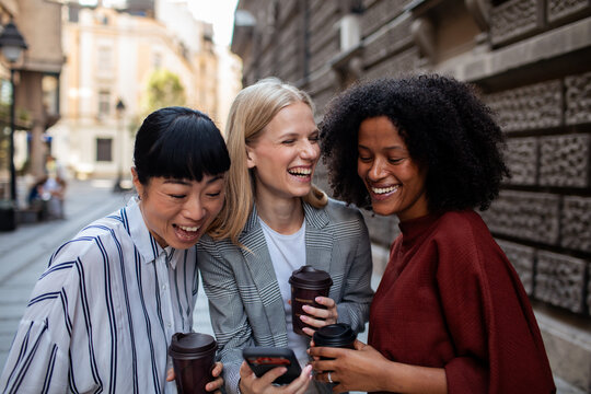 Three women friends laughing at a smartphone on a city street