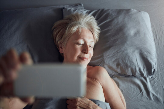 Smiling senior woman taking selfie in bed at home
