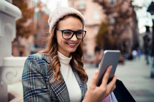Smiling woman using smartphone on city street in autumn