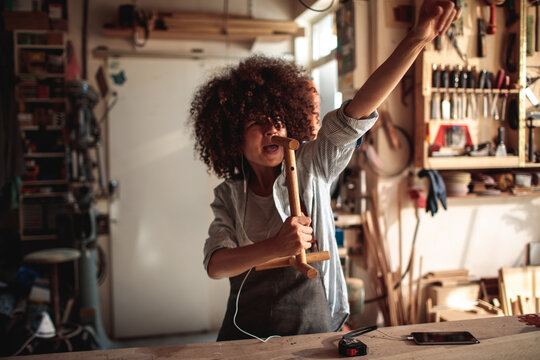 Woman woodworker singing with earphones in carpentry workshop