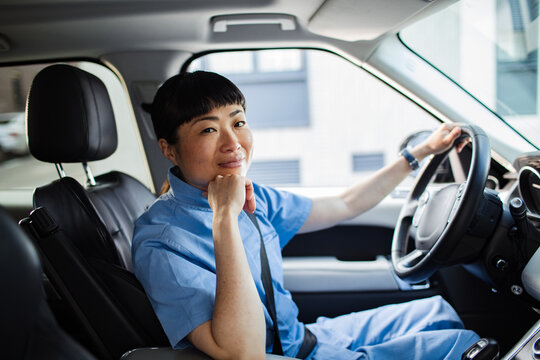 Smiling healthcare worker in scrubs driving car in city