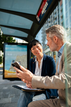 Two business colleagues using smartphone at urban bus stop