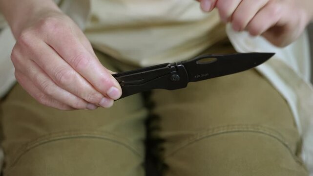 Woman's hands opening black folding pocket knife. Close up view of female hands opening a black steel folding pocket knife, demonstrating the mechanism and revealing the sharp blade for everyday carry