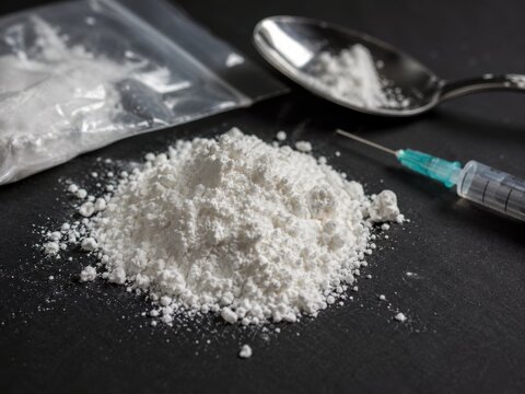 A pile of white powder, a syringe, and a spoon with powder on a dark background represent drug use.