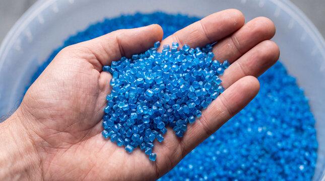 A close-up of a human hand holding blue plastic resin pellets used in industrial injection molding and plastic manufacturing processes.