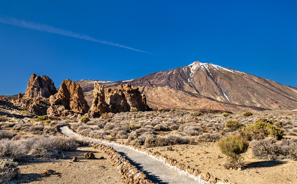 A scenic hiking path leads towards the volcanic rock formations of Roques de Garcia and Mount Teide in Teide National Park, Tenerife, Spain.