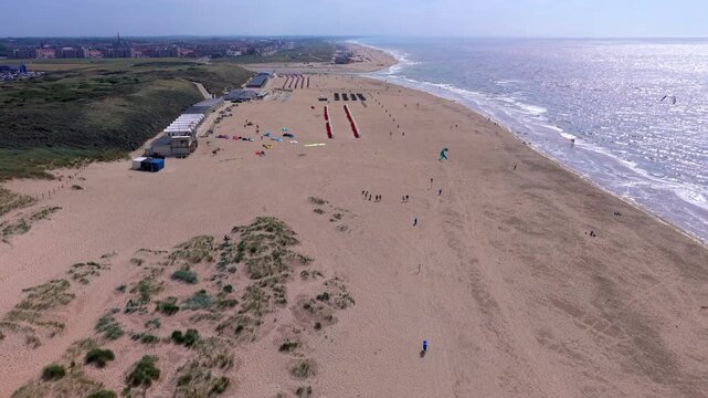 Aerial view video clip of Katwijk aan Zee beach in Netherlands, featuring kitesurfers, beach cabins, sand dunes, and sparkling North Sea under bright sunlight