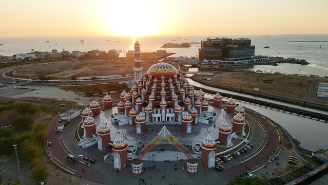 Aerial view of Masjid Kubah 99 Asmaul Husna with colorful domes and minaret, situated along the waterfront during sunset in Kecamatan Mariso, Sulawesi Selatan, Indonesia.