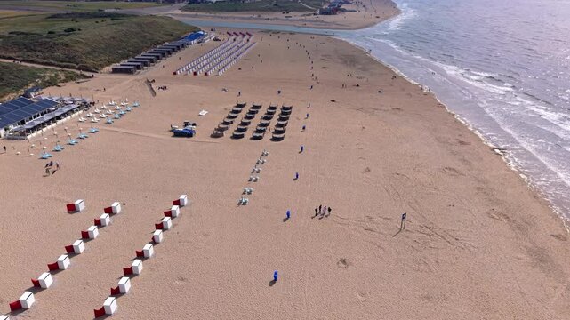 Aerial view video clip of Katwijk aan Zee coastline in Netherlands, featuring colorful beach cabins, sun loungers, sand dunes, beach pavilion, and North Sea horizon on a sunny day