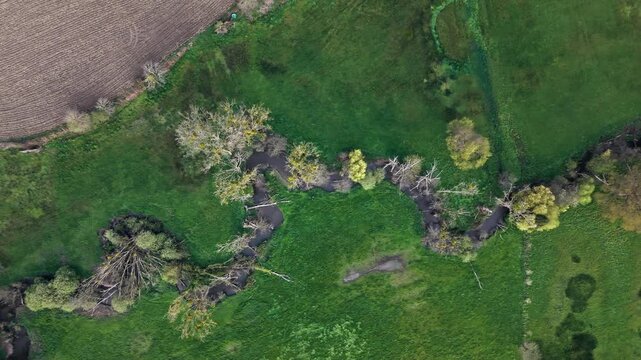 Aerial top down view of narrow winding river crossing green countryside. River shape forms natural pattern in rural Normandy landscape