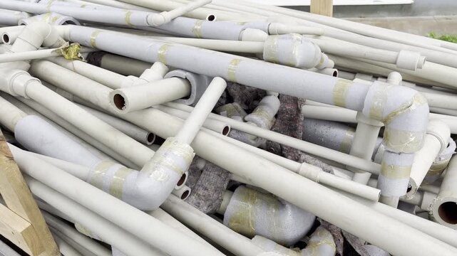 A pile of disassembled plastic water pipes with foam thermal insulation lies stacked outdoors. These plumbing materials are collected and prepared for waste management