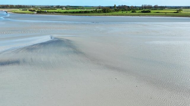 Broad Normandy tidal flats revealed by low tide, showing natural sand patterns, shallow channels and calm coastal scenery