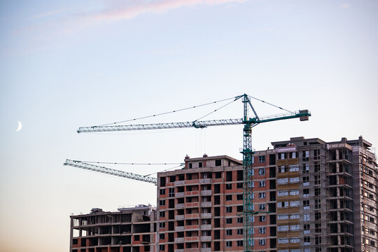 Modern residential building construction site with cranes under evening sky and crescent moon