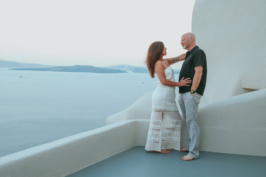 Middle‑aged couple enjoying a quiet moment together on a white terrace overlooking the Aegean sea at Santorini, Greece during sunset.