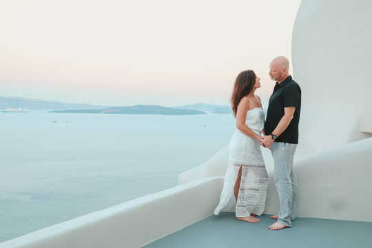 Middle‑aged couple enjoying a quiet moment together on a white terrace overlooking the Aegean sea at Santorini, Greece during sunset.