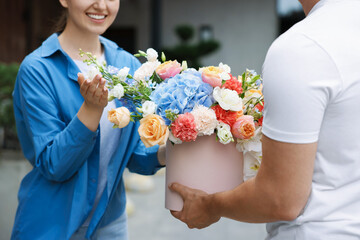 Courier giving beautiful bouquet of flowers to woman outdoors, closeup