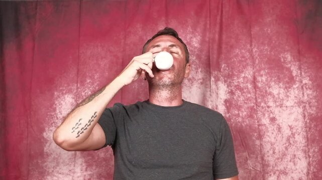 A man drinks an Italian coffee from a small white porcelain cup. The man is forty-two years old, has short hair and a short beard and wears a dark T-shirt