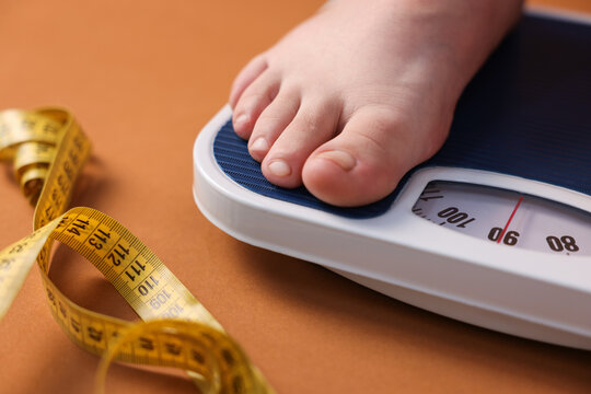 Overweight woman on scale and measuring tape against brown background, closeup