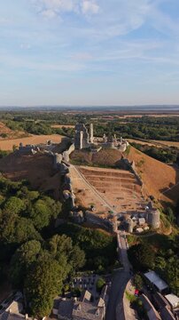 Aerial drone footage of the iconic Corfe Castle in Dorset, England, showcasing the medieval castle ruins, historic village, and rolling Purbeck countryside on a hot summer morning