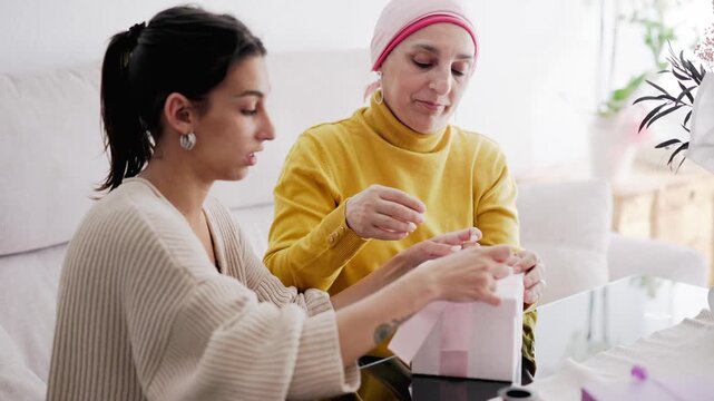 Supportive daughter assisting mother with cancer wrapping gift box