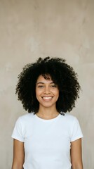 Fototapeta premium Young woman with dark curly hair and warm smile wearing white t-shirt against neutral beige background, suitable for portrait, diversity, lifestyle and professional headshot applications.