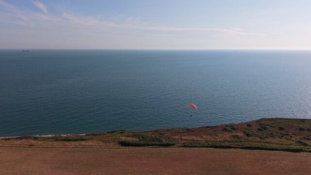 Aerial drone footage of a paraglider flying along the south coast of the Isle of Wight at sunset. The scenic coastal landscape, English Channel, cliffs, and warm golden-hour light