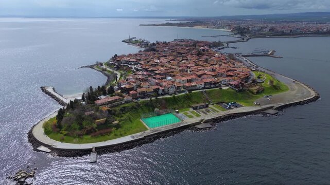 Aerial view of the historic Old Town of Nessebar, Bulgaria, occupying a compact Black Sea peninsula filled with red-tiled roofs, traditional buildings, churches, waterfront roads and protective breakw