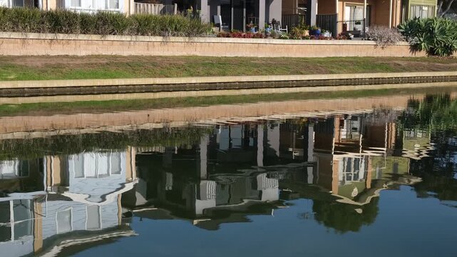 Modern waterfront suburban houses and concrete retaining walls reflecting on the calm and peaceful surface of a waterway. Sanctuary Lakes, Point Cook, Melbourne Australia. Upscale housing estate