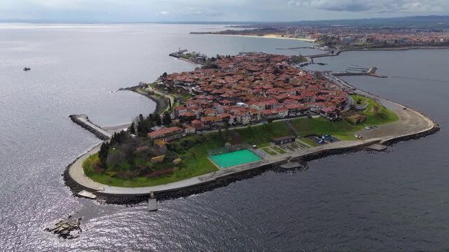 Aerial view of the historic Old Town of Nessebar, Bulgaria, occupying a compact Black Sea peninsula filled with red-tiled roofs, traditional buildings, churches, waterfront roads and protective breakw