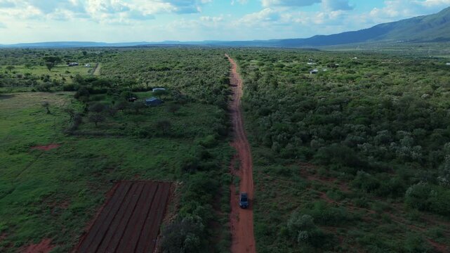 Aerial view of a vehicle driving along a red dirt road through the lush green landscape of Ngong Hills in Kajiado County, Kenya.
