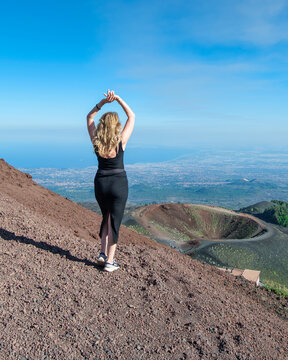 Rear view of a woman standing with her arms above her head looking at the  Volcanic cinder cones and craters on Mt Etna, Catania, Sicily, Italy