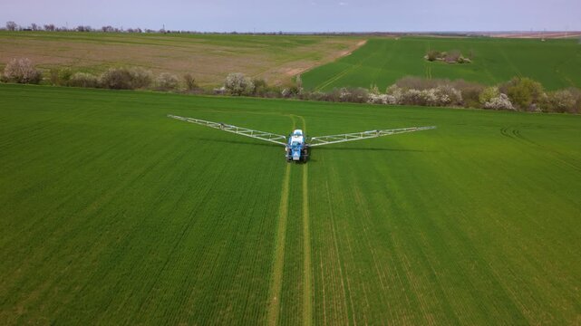 Aerial view of a self-propelled agricultural sprayer moving across a green crop field with its wide boom fully extended, showing modern precision farming and large-scale crop treatment.