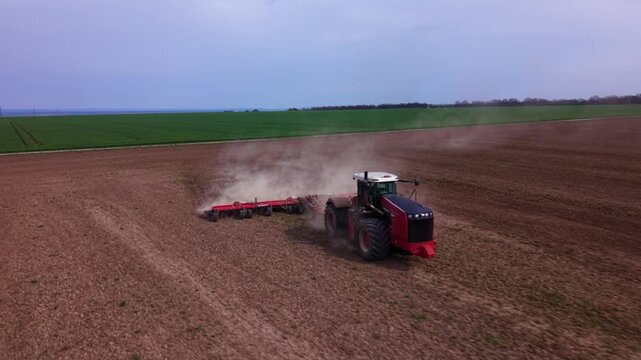 Aerial view of tractors performing field preparation and precision planting across a large cultivated agricultural field, using wide implements that create parallel rows and raise dust behind the mach