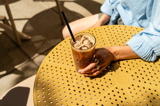 Close-up of a stylish Woman sitting at an outdoor cafe table holding an iced espresso tonic drink
